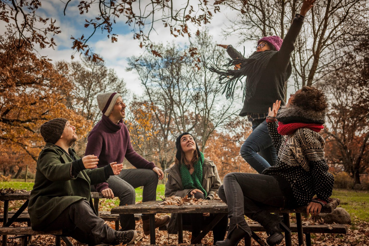 Group of twenty-somethings laughs it up in the park on a Fall day.